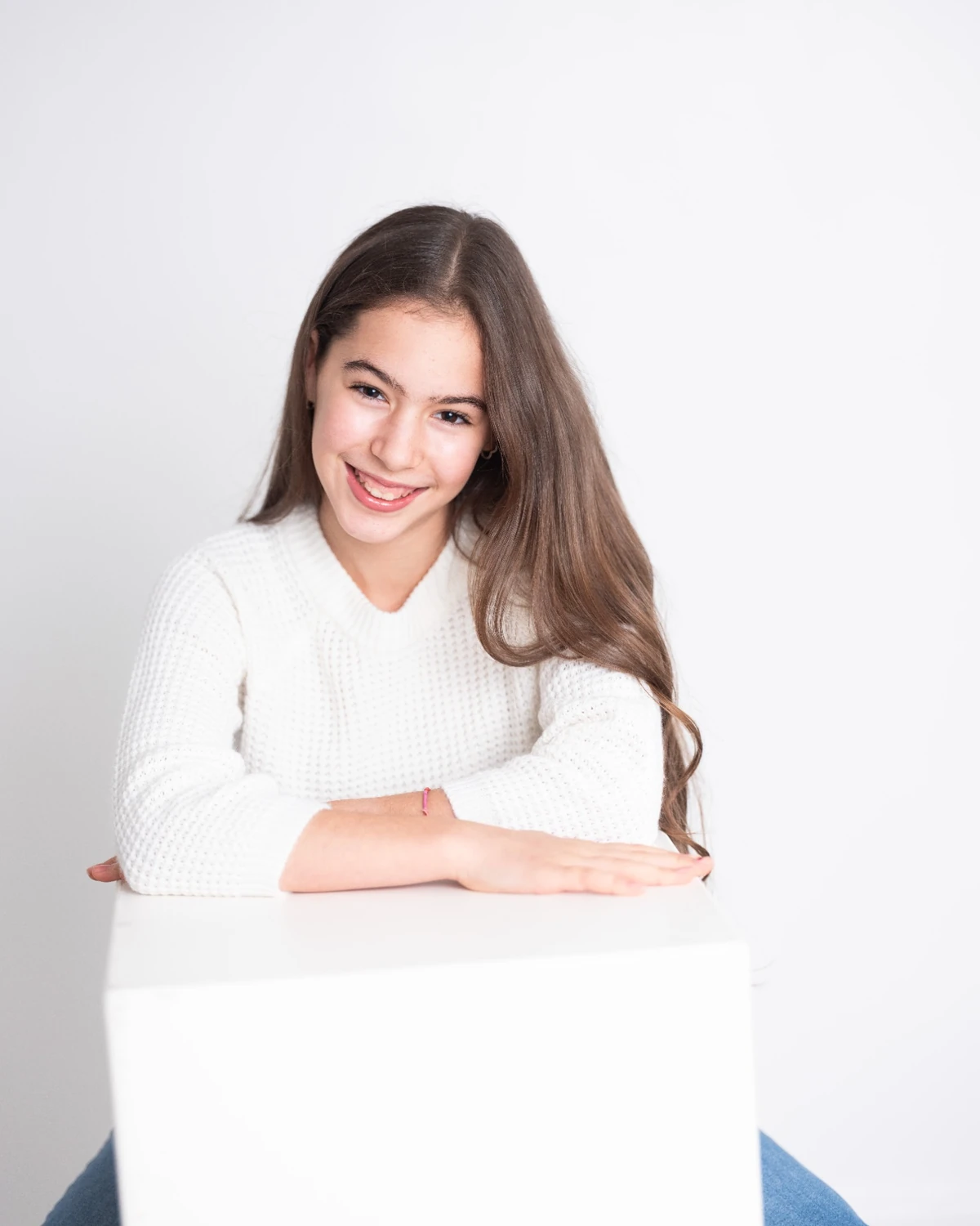 Samara in a white sweater leaning on a white cube
